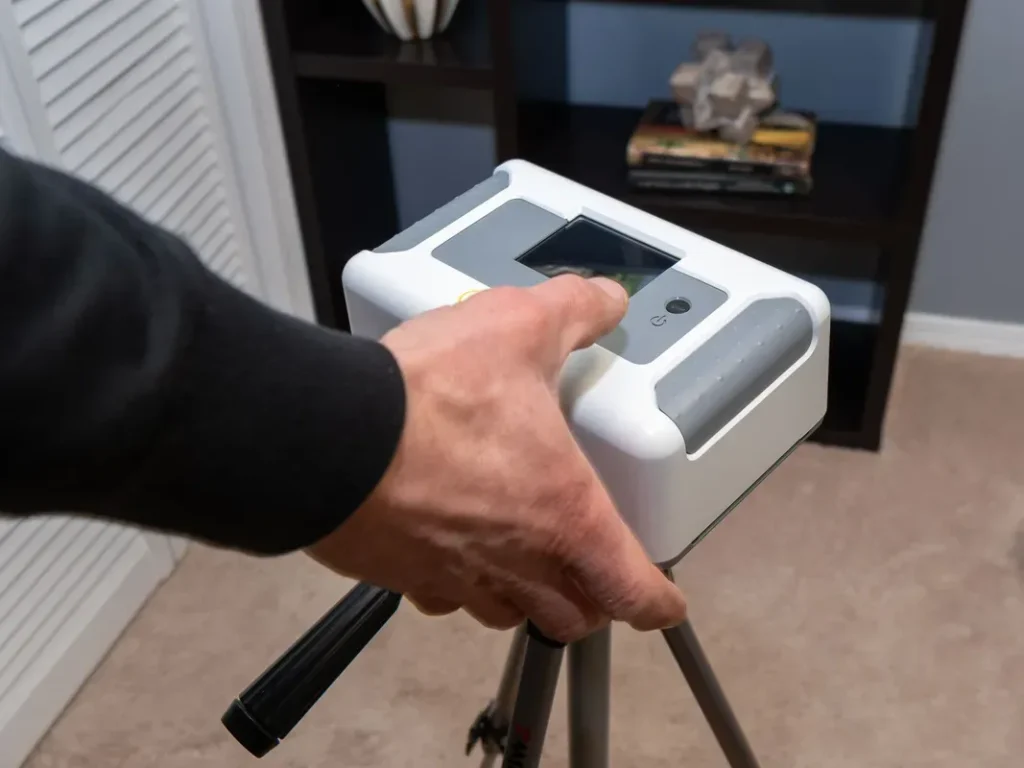 A hand adjusting an air quality monitor on a tripod, used for property assessments