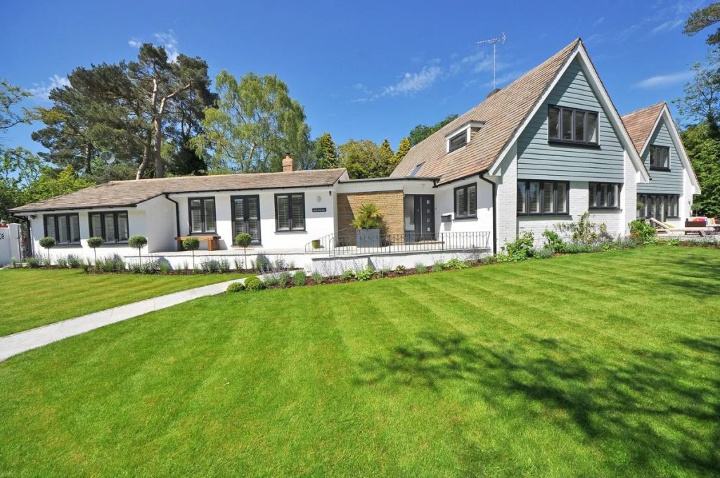 A modern white house with a green lawn under a blue sky, representing a property for inspection