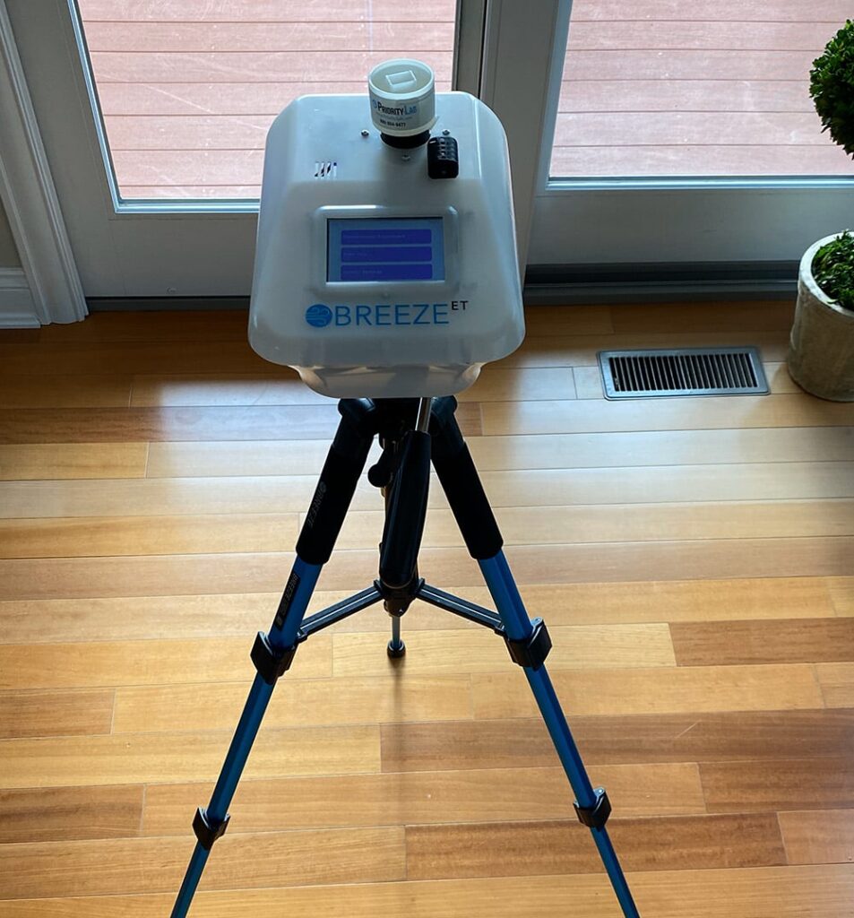 Breeze ET air sampling system on a tripod, positioned on a hardwood floor near a glass door