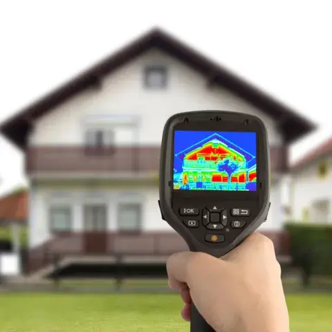 Hand holding a thermal imaging camera displaying a house with red and blue heat signatures