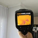 Hand holding a thermal imaging camera showing a ceiling with orange and purple heat signatures